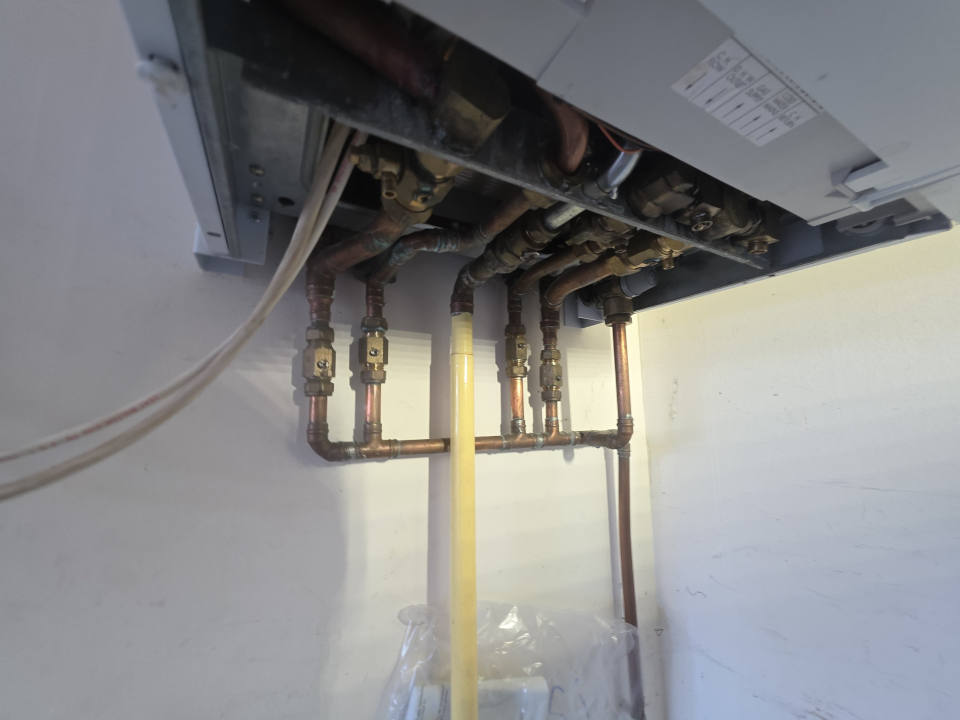 Copper and plastic pipework with isolation valves below a wall-mounted boiler.